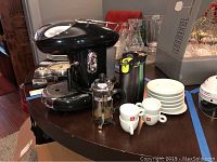 Overview of espresso machine, cups, saucers, press, and travel decanters on wooden table