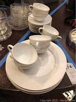 Top view of stacked white porcelain cups and saucers with silver rims, along with white dinner plates underneath.