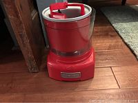 Front view of the red Cuisinart ice cream maker showing control panel and clear mixing lid with red paddle inside.