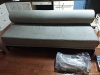 Full view of grey sofa with rolled headrest and sealed extra fabric bag on floor