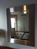 Front view of the rectangular wall mirror hung on a wall reflecting room interior.
