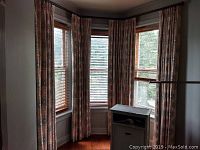 Four blackout fabric drapes hung on windows, showing the size and pattern of the curtains in use, and a corner of a room's interior.