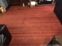 Full view of the large reddish-brown custom cut rug in the room showing its size and clear surface.