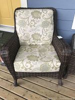 Front view of dark brown wicker patio chair with cream and green floral patterned Sunbrella cushions.