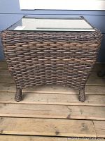 Front view of the Ratana wicker patio end table showing woven wicker texture and curved legs on wooden deck.