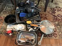 Overview of assorted kitchen cookware, utensil collection, including pans, spatulas, and a blender attachment on floor