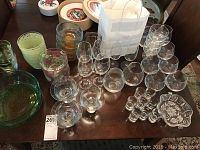 Photo showing assorted glass bowls, tumblers, shot glasses, and a set of 8 crystal wine stems on a table.