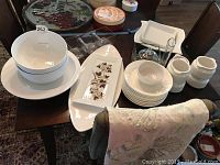 Full view of assorted white ceramic dishes and decorative items arranged on table, with a beaded butterfly table runner visible.