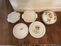 Five kitchenware pieces including Royal Worcester Evesham Vale covered casserole, Corning Ware covered casseroles, and two ceramic pie plates shown together on floor.