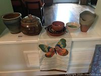 Full set of pottery on a white surface including a greenish-blue plant pot, the bean pot with lid, three small bowls of varied glazes, and an 8-inch pottery vase. Front-laying embroidered butterfly table runner