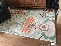 Full view of wool area rug with colorful floral pattern placed on hardwood floor.