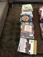 Overview of multiple cookbooks laid out on a surface, including Windows on the World Complete Wine Course, a pizza cookbook, and others featuring various dishes.