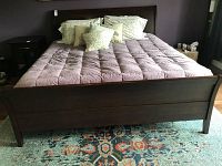 Front view of king size wooden bed frame with dark finish, showing headboard, footboard, and mattress covered by bedding.