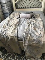 Two embroidered linen curtain panels laid over a bed, showing the paisley embroidery detail and natural linen color.