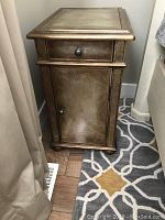 Single night stand showing drawer, door, and distressed gold finish on carpeted floor.