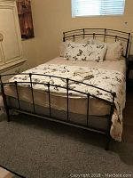 Full view of assembled queen sized black metal bed frame dressed with bedding including duvet, quilt, and pillows with butterfly motifs.
