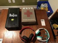 Overall lot contents including The Beatles box, M*A*S*H DVD box, and two headphones on table.