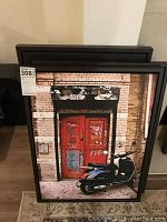 Framed canvas print showing urban red door with graffiti and scooter parked in front, stacked behind two other similar prints