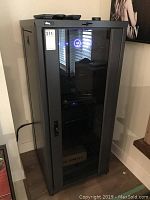 Closed metal electronics cabinet with glass door, showing the reflective glass and cabinet design