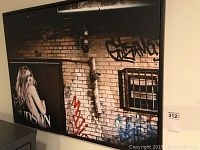 Framed canvas print showing the woman in front of graffiti-covered brick wall.