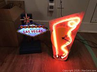 Both items shown illuminated: the desk lamp with colorful Las Vegas sign and the neon clock with red glowing design and clock hands on the wooden floor.