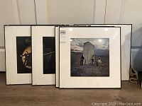 Set of six framed album covers stacked against a wall, showing white mats and black frames.