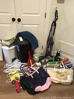 Full lot contents showing assorted household and laundry items including plastic hangers, umbrellas, cleaning supplies, waste bins, dustpans, totes and vacuum
