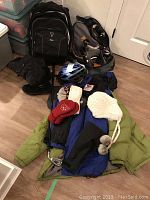 Photo showing a collection of winter jackets, assorted winter hats, gloves, mittens, backpacks, a bicycle helmet, rollerblades, golf club shaft.