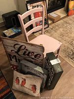Photo showing pink wooden chair with ladder back design alongside wooden Live Music sign and other decor items clustered.