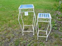 Pair of two metal and wood plant stands side by side on grass, one taller with blue slatted top and white metal frame.