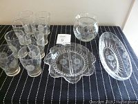 Full set displayed on black fabric including eight etched glasses, one vase, two serving dishes with cornflower patterns.