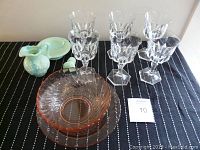 Grouped view of six clear wine glasses, pink swirl glass bowl and platter, Avon green mini pitcher and bowl on black cloth