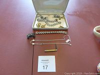 Wide view of all items including open jewelry case with rhinestone necklace and bracelet, several bracelets and necklaces on table, three sets of cufflinks, metal carriage toy, and penknife