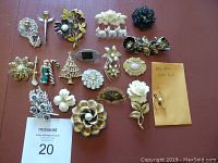 Full view of 23 assorted brooches laid flat on a brown background, showing wide variety of styles including floral, animal, holiday and decorative designs.