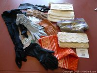 View showing all six pairs of gloves, three pairs in original packaging, three vintage clutch purses with textured and lace detailing, and two scarves.