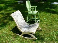 Antique nursery rocking chair with floral vinyl upholstery and green painted wooden high chair in outdoor setting shown from side angle.