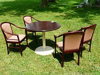 Full view of the round wooden table with cast iron pedestal base and four matching vinyl upholstered armchairs arranged around it on grass.