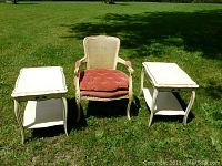 Full view of French Provincial style caned back chair with cushion and two matching side tables placed on grass.