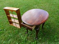 Broyhill oval side table with claw feet and drawer next to wooden three shelf wall hanging display shelf outdoors on grass