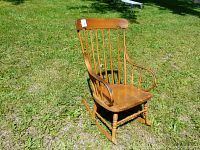 Wooden rocking chair angled view showing seat, back, curved armrests, and rocker runners on grass