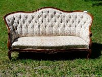Front view of Victorian style sofa showing button tufted floral upholstery and carved wooden frame