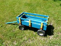 Photo of a blue painted wooden kids wagon with sides, worn paint, rubber wheels on grass