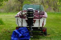 Rear view of white fiberglass boat with Mercury outboard motor mounted on metal trailer. Blue tarp under motor.