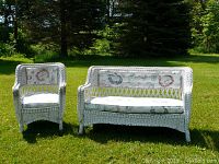 Front view of white wicker loveseat and armchair with cushions on grass