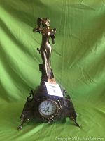 Front view of clock showing figural female statue and marble base with metal feet