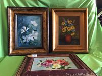 Front view of the three framed floral oil paintings arranged against green fabric background showing frame styles and overall condition