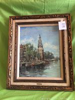 Full view of the framed vintage oil painting showing a scenic riverside with boats and buildings under a partly cloudy sky.