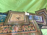 Top view showing multiple embroidered oriental fabric pieces overlapping on a green backdrop. Various colors and intricate patterns visible.