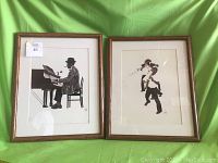 Framed art prints standing side by side on green fabric background showing both jazzy musicians in silhouette style with wooden frames