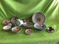 Overall view of the 12 assorted Oriental pottery items arranged on green fabric.
